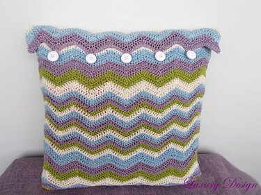 Gehäkelter Kissenbezug in Pastellfarben mit Zickzackmuster und weißen Knöpfen
