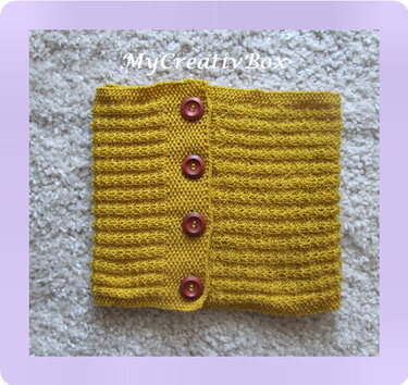 Senfgelber gestrickter Loop-Schal mit vier braunen Knöpfen auf hellem Untergrund