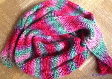 Gestricktes Dreieckstuch mit rot‑pink‑grünem Farbverlauf und Lochkante auf Holzuntergrund