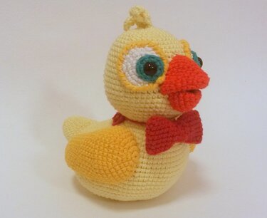 Seitenansicht eines gelben gehäkelten Amigurumi-Kükens mit roter Fliege