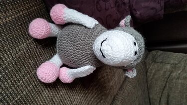 Handgehäkeltes, lächelndes Amigurumi-Pony in Grau und Rosa auf einer Stoffoberfläche
