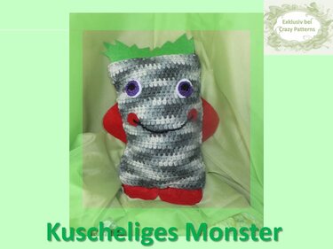 Gehäkeltes rechteckiges Kuschelmonster-Kissen, grau-weiße Streifen, lila Augen, rote Filzdetails, grüne Zacken