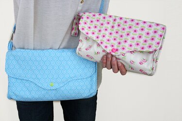 Person trägt blaue Crossbody-Tasche und hält weiße Clutch mit Blumenmuster.