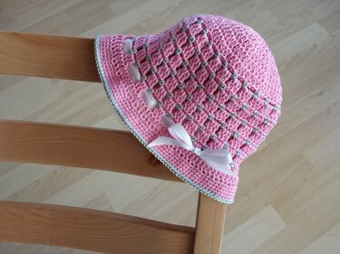 Rosa gehäkelte Babymütze mit weißer Schleife auf Holzstuhl