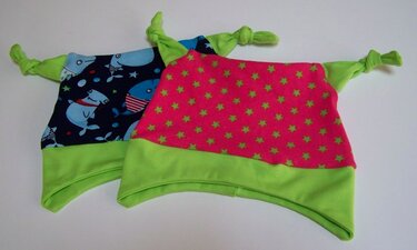 Zwei genähte Knotenmützen für Baby oder Kind, eine mit Walmuster und eine mit Sternenmuster.