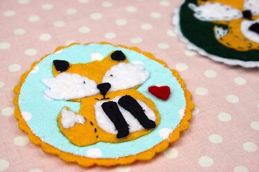 Runde Filz-Applikation: orange-weißer Fuchs mit rotem Herz auf hellblauem Punktestoff und gelbem Wellenrand auf rosa Untergrund.