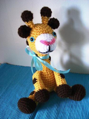 Gehäkelte Amigurumi-Giraffe mit Flecken, weißer Schnauze und hellblauer Schleife