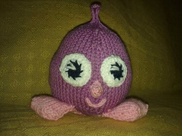 Gestricktes lila Amigurumi mit weißen Augen und rosafarbenen Füßen
