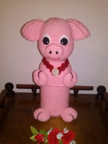 Stehendes rosa Amigurumi‑Schwein mit zylinderförmigem Körper, applizierten Augen und rotem Knopf‑Halsband