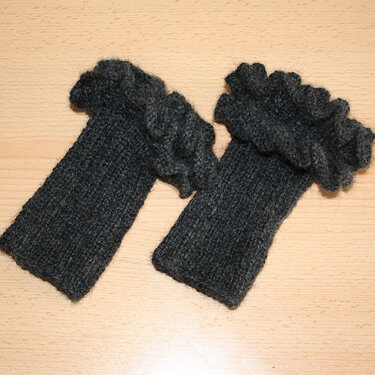 Zwei dunkelgraue gestrickte Armstulpen mit Rüschenbündchen auf Holzuntergrund