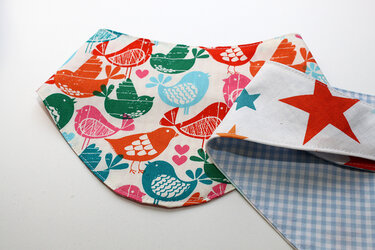 Wendbares Babybandana mit Vogelprint auf der einen Seite und roten Sternen auf der anderen, sichtbare Nahtkante