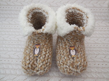 Beige-weiß gestrickte Hausschuhe mit weißem Plüschrand und Eulen-Applikationen auf hellem Strickstoff.