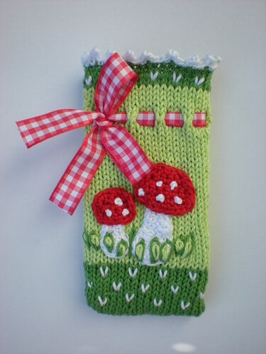 Handgestrickte hellgrüne Hülle mit roten Fliegenpilzen und rot-weiß kariertem Band