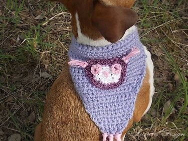 Brauner Hund mit gehäkeltem lila Halstuch mit rosa-weißer Blütenapplikation und Fransen