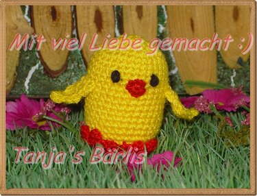 Gelbes gehäkeltes Amigurumi-Küken mit roten Füßen und schwarzen Augen auf Gras