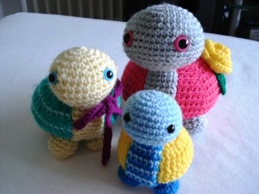 Drei gehäkelte Amigurumi‑Schildkröten in verschiedenen Größen und Farben, eine mit gelber Blume auf dem Panzer.