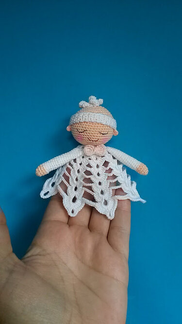 Hand hält weißes gehäkeltes Schmusetuch mit kleinem Puppenkopf