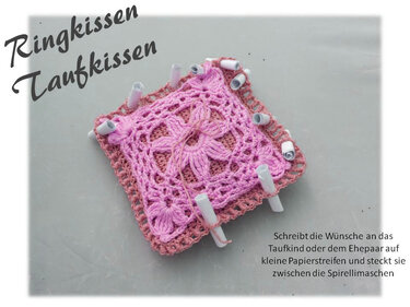 Quadratisches, handgehäkeltes pinkes Kissen mit floralem Muster und weißen Röhrchen in Spiralmaschen für eingerollte Wunschzettel.