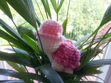 Mini gehäkeltes Tier mit rosa Hut und pinker Rückseite zwischen Pflanzblättern