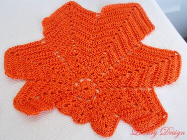 Orangefarbenes gehäkeltes Deckchen mit Zacken- und Lochmuster auf hellem Untergrund