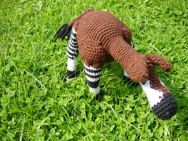 Gehäkeltes Okapi-Amigurumi mit braunem Körper und schwarz-weißen Streifen an den Beinen auf grüner Wiese