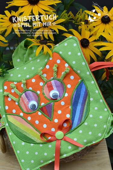 Selbstgenähtes, buntes Knistertuch in Eulenform mit Wackelaugen und weißen Punkten vor gelben Blumen