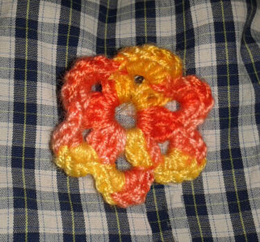 Gehäkelte Blume in Orange und Gelb auf blau-weiß kariertem Stoff