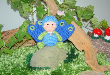 Referenzfoto kleines Pfauen-Amigurumi mit blau-grünen Flügeln und Aufhängeschlaufe