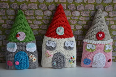 Drei handgehäkelte Amigurumi-Häuser mit bunten Dächern und Verzierungen