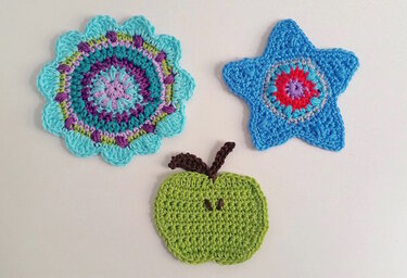 Drei gehäkelte Applikationen: türkis-lila Mandala, blauer Stern und grüner Apfel.