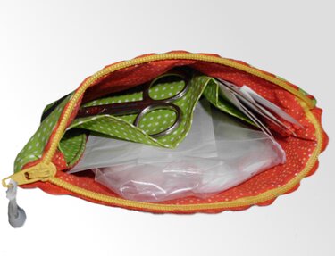 Offene orange Stoff-Utensilo-Tasche mit gelbem Reißverschluss, grünem Inneneinsatz, Schere und Folienbeuteln