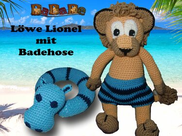 Gehäkelter Amigurumi-Löwe mit blauer gestreifter Badehose neben türkisfarbenem Schwimmring vor Strandhintergrund