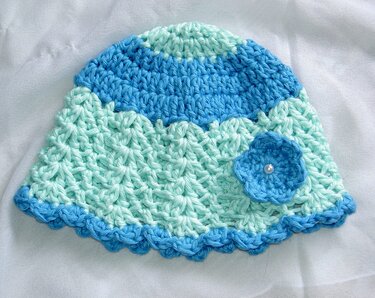 Gehäkelte Babymütze in Mint und Blau mit Wellenrand und kleiner Blume mit Perle.
