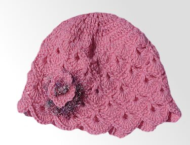 Rosa gehäkelte Babymütze mit Muschelmuster und Blumenapplikation mit leichtem Glitzereffekt an der Seite.