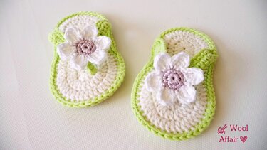 Paar gehäkelter Babysandalen cremeweiß mit grüner Kante und weißer Blüte