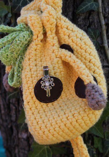 Gehäkelter gelber Zuziehbeutel mit Giraffenohren, grünen Kordeln und Metallclip