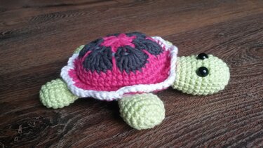 Gehäkelte Amigurumi-Schildkröte mit pink-grauem Panzer auf Holz