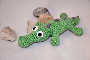 Gehäkeltes grünes Amigurumi-Krokodil mit weißen Augenrändern, liegend