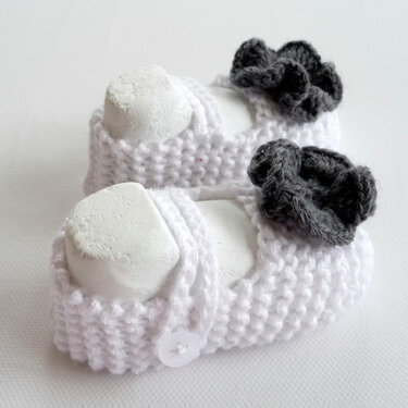 weiße gestrickte Babyschühchen im Ballerina-Stil mit grauer Blüte und Knopfriemen