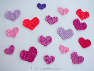 Gehäkelte Herz-Applikationen in Rosa, Lila und Rot auf hellem Hintergrund.