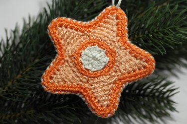 Gehäkelter fünfzackiger Sternanhänger in Orange und Creme an Tannenzweig