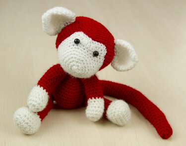 Sitzender gehäkelter Amigurumi-Affe, rot mit weißen Ohren, Schnauze und Pfoten.