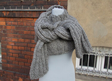 Grauer grob gestrickter Pullover mit voluminösem, vorne geknotetem Schalkragen auf einer Schaufensterpuppe.