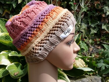 Gestrickte Damenmütze in Pastellstreifen mit Ajourmuster auf Schaufensterpuppe vor Grünpflanzen