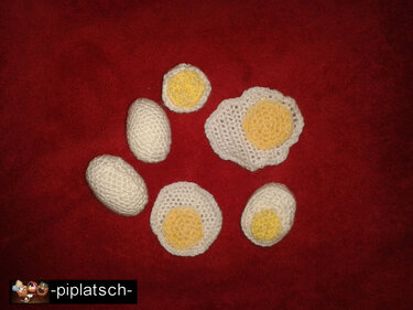 Gehäkelte weiße und gelbe Spiel-Eier und Spiegelei auf rotem Stoff
