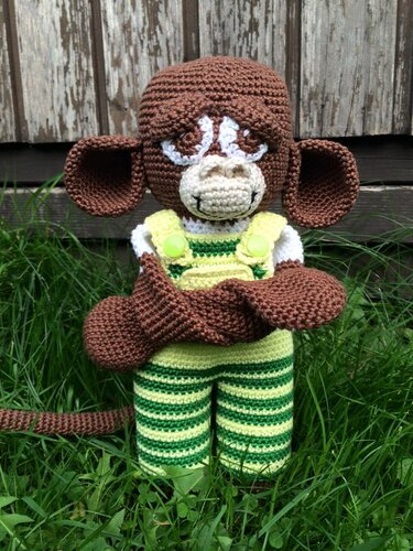 Brauner gehäkelter Amigurumi-Affe mit grün-gestreiftem Overall auf Gras