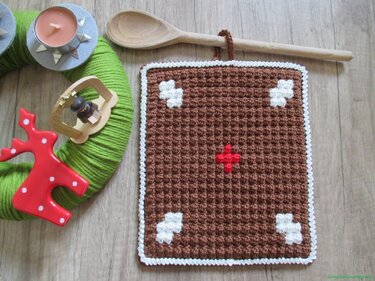 Brauner gehäkelter Topflappen im Lebkuchen-Design mit weißen Mustern und rotem Kreuz
