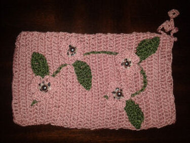 Rosa gehäkeltes Täschchen mit drei Blumenapplikationen, grünen Blättern und Perlen