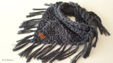 Dunkelgraues gehäkeltes Dreieckstuch mit langen Fransen auf hellem Hintergrund