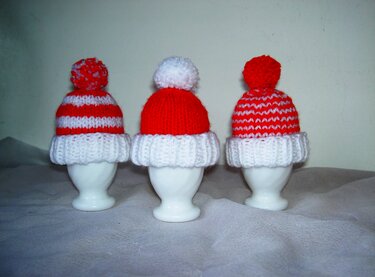 Drei gestrickte rot-weiße Eierwärmer mit Bommel auf weißen Eierbechern